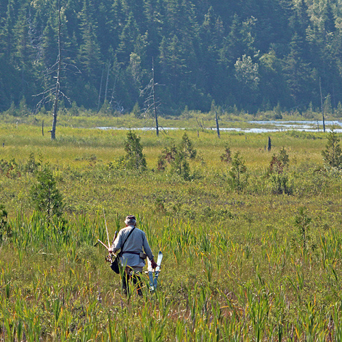 A fisherman heads through a bog and towards a remote lake in rural New Brunswick.