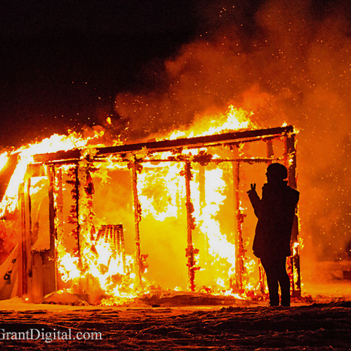 A passerby flashes the peace sign as an ice shack meets a fiery end.