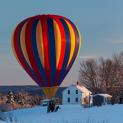 As the sun slowly sets, a hot air balloon gets escorted across a farmer's field and towards a proper spot to collapse…