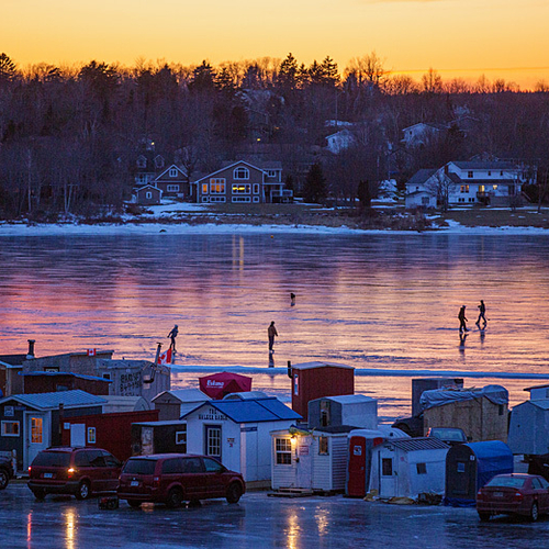 Renforth ice huts at twilight with ice skaters and the homes of Kennebecasis Park in the background.