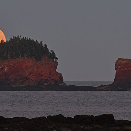 The full harvest moon peeks over Split Rock in rural Saint John County, New Brunswick, Canada.