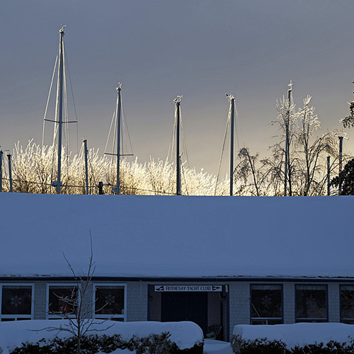 Masts of sailboats in winter storage glitter in the early morning sunlight behind the RYC clubhouse in Rothesay, New…