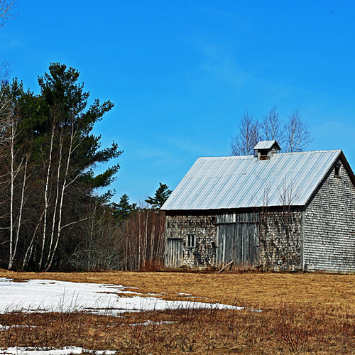 Remnants of snow add contrast to a blue spring sky and heritage barn.