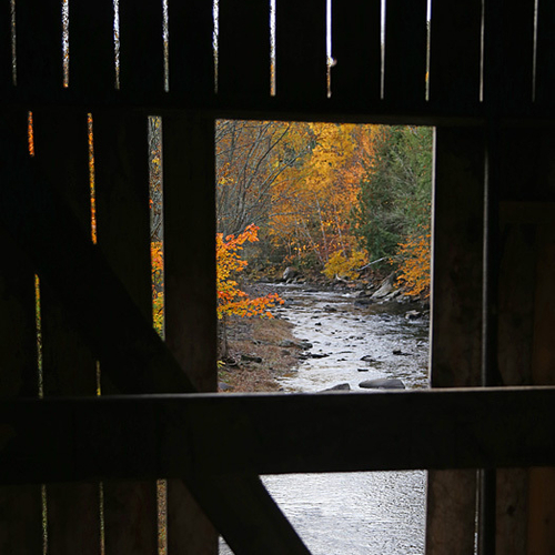 Autumn color filters through a covered bridge's wooden slats in rural New Brunswick, Canada.
