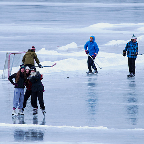 A trio of skaters pause for a pose while a game of shinny carries on in the background.