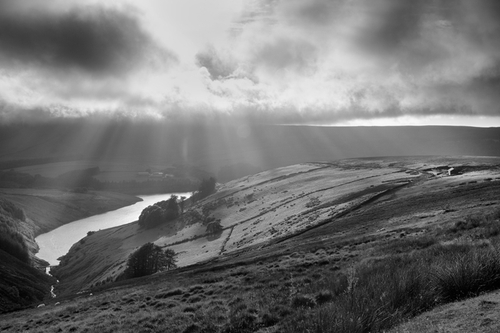 Rays of light poking through the changeable sky on a breezy day looking over the Sulby Reservoir.