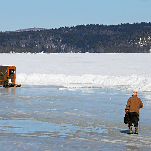 An ice fisherman heads towards a lone shack.