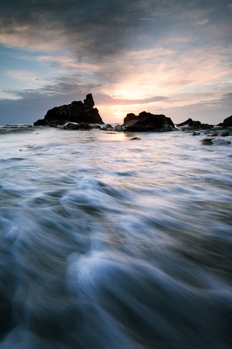 The sun sets through the gap between the rocks at White Beach at the end of a stormy summer day.