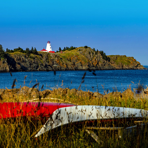 Overturned canoes in overgrown grass create a lazy day's ambience at Pettes Cove, Grand Manan with historic Swallowta…