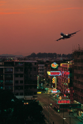 KM-172B Plane flying into Kai Tak over Kowloon city at dusk - 1985