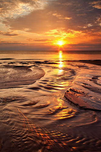 The sun sets just of Jurby with the water weaving its way to the sea. The light catching the ripples and resembling g…