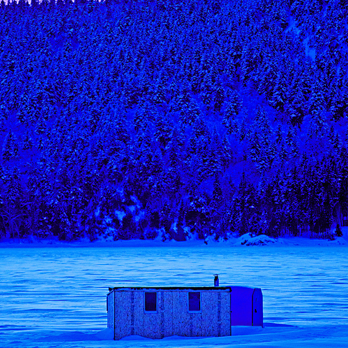Ice shack along the Kennebecasis River with snow-capped hillside in the backdrop.