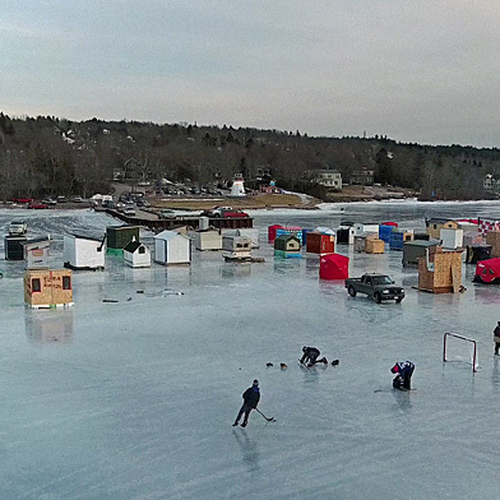 A pond hockey game plays on along the Kennebecasis River and behind the ice shack village @ Renforth in Rothesay, NB,…
