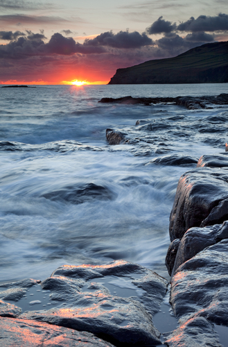A firery red November setting sun reflects of the wet rocks at Port St. Mary.