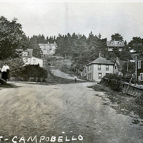 A lady stands at the end of a driveway while a man approaches on a bicycle in this early 1900s view of Campobello Isl…