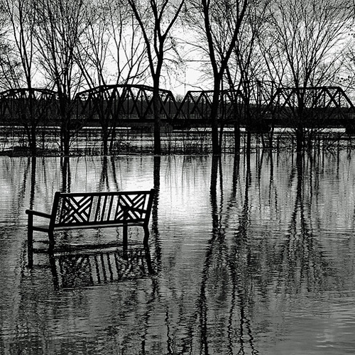 Park Bench on dead calm Sunday morning lies dormant and empty in the midst of the great spring flood of 2018 in New B…
