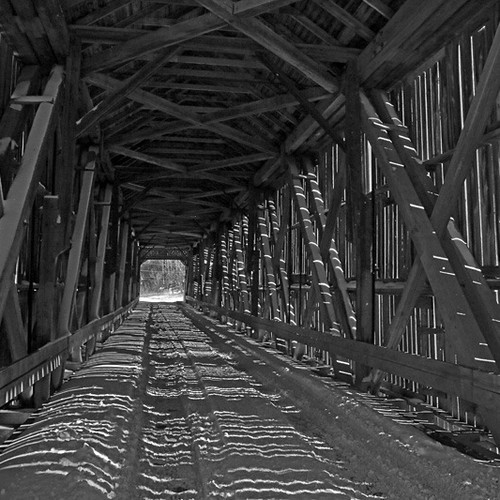 A b&W of the interior of a covered bridge just after a snowstorm.