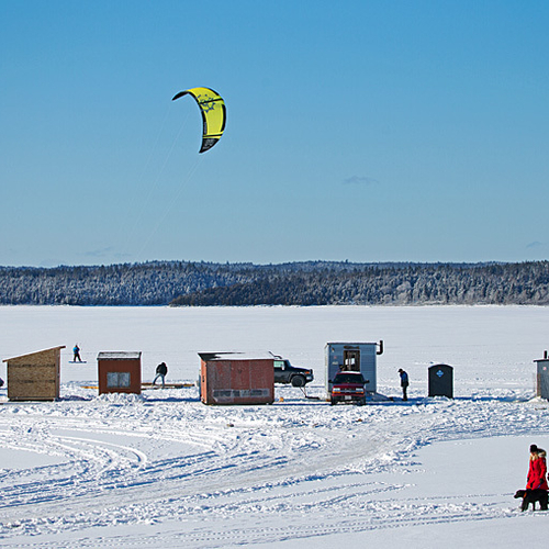A snowkiter breezes past the 'under construction' ice village as a couple strolls past with their dog on opening day,…