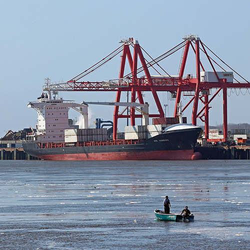 Fisherman set their tackle while a large cargo ship does business in the background.