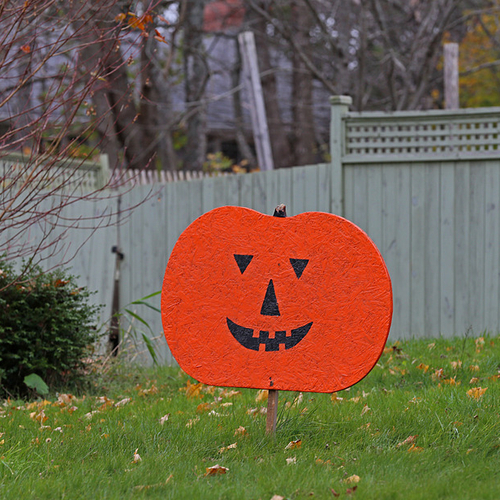 A carved wooden 2d pumpkin awaits the festive eve in a residential front yard.