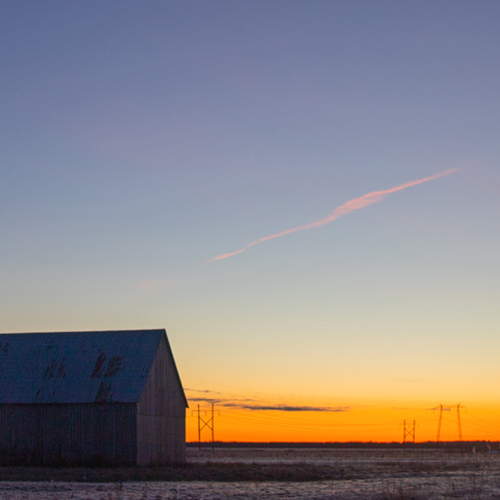 A hay barn at sunrise looms large against the flat marshlands of Tantramar.