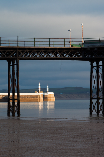 Early morning sunlight catches the lighthouses at the entrance to Ramsey Harbour. The pair of gulls perched on Queens…