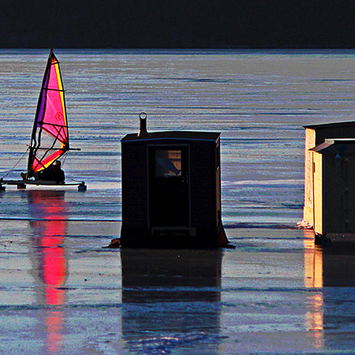An iceboat sails by ice fishing shacks at Renforth, NB.