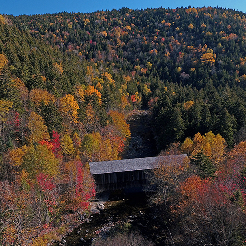Aerial POV of the Crooked Creek Covered Bridge amid peak autumn foliage.