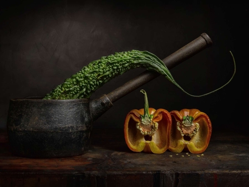 Bitter Melon. Light-painted still-life photograph of a Bitter Melon fruit, cut pepper and vintage saucepan. Lit by di…