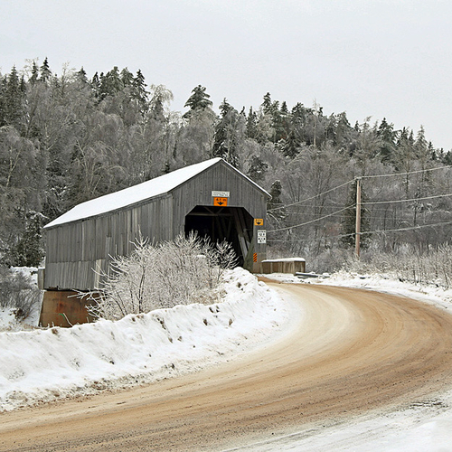 A Covered bridge along a country road in wintertime.
