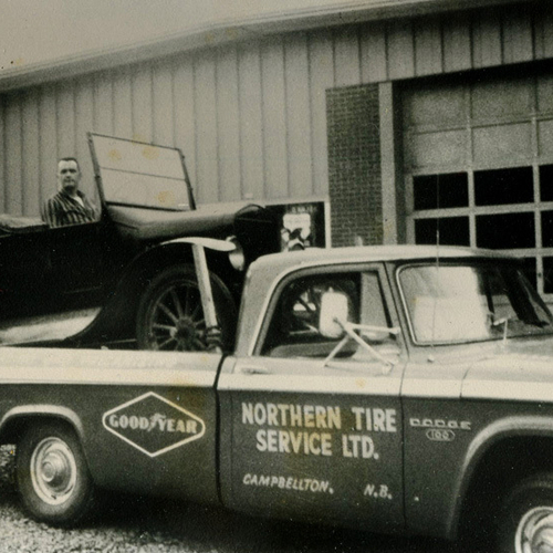 Circa 1960s picture of a Northern Tires Service's Dodge D100 truck with vintage vehicle in tow.