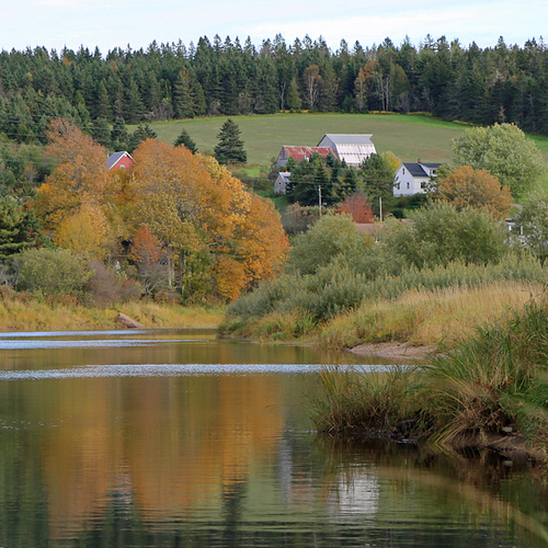 A farmhouse nestled away on a hill & near a waterway is a common sight in Maritime Canada.