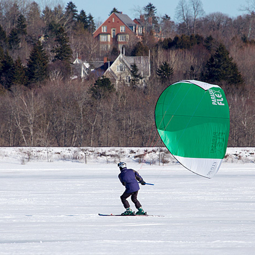 A snowkiter sails along the Kennebecasis River with the buildings of Rothesay Netherwood School in the backdrop.