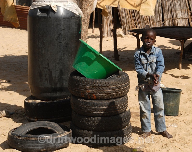 Senegal Fulani Village Fulani boy standing by tyres - Senegal Fulani Village
