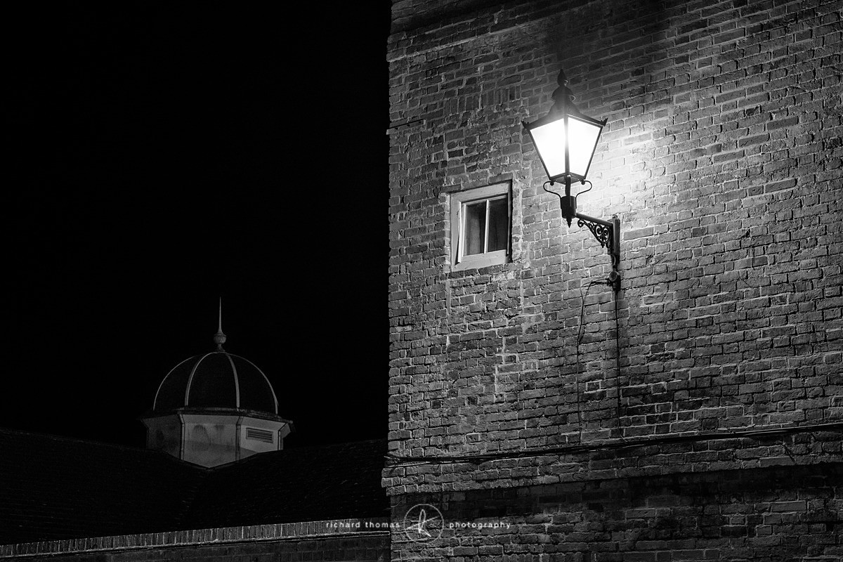 An old street lamp on the side of a building in Farnham Surrey at night