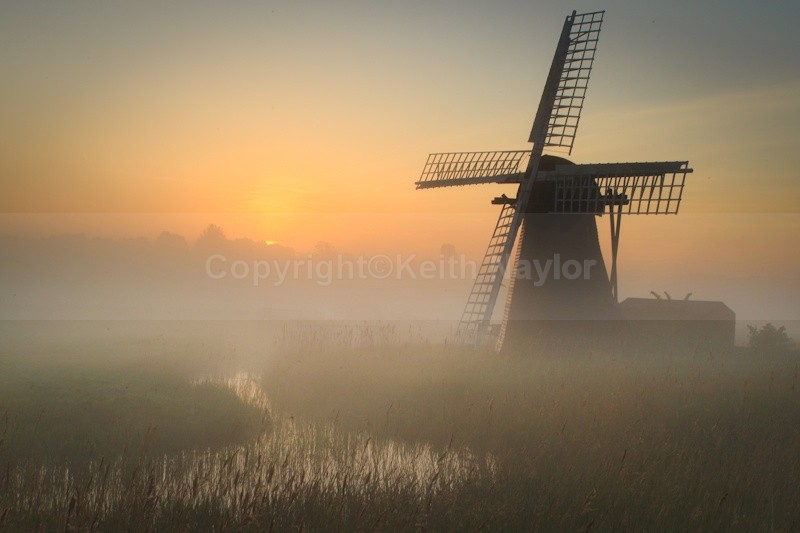 Windmill at dawn with sun rising in the east over a misty marsh