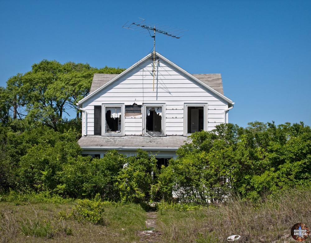 A forlorn white home swallowed by trees