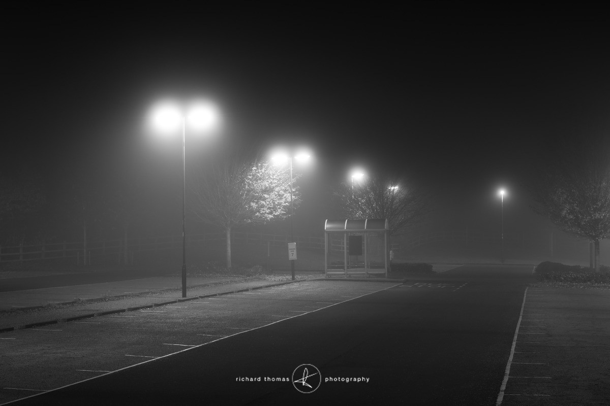 An empty shelter by a car park bus stop at night