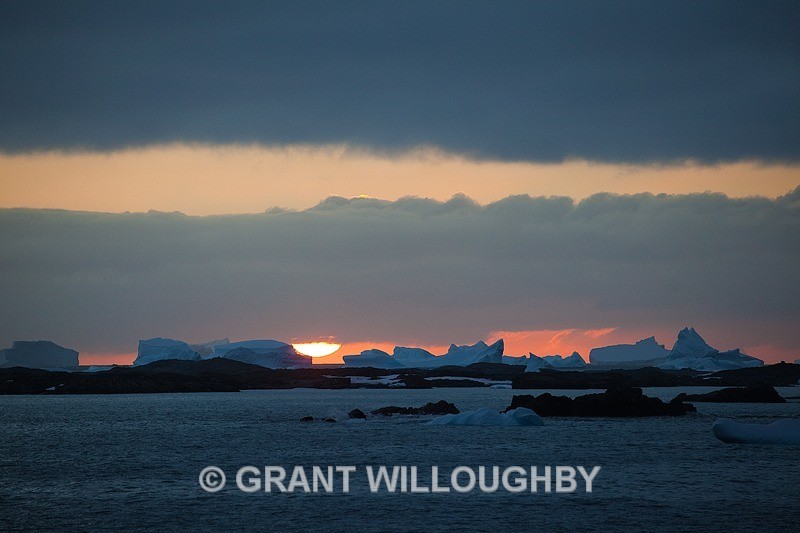 The sun sets behind the icebergs - Antartica